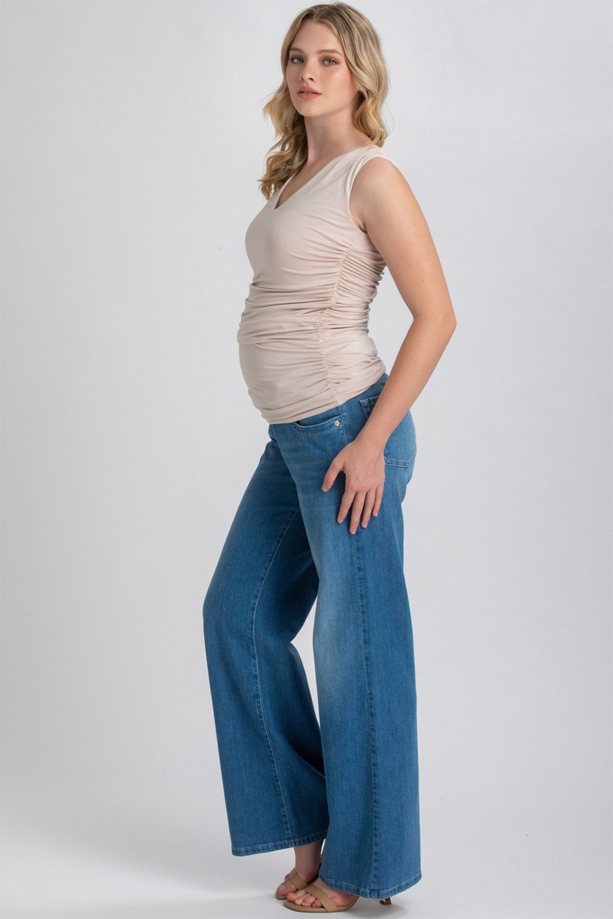 Modella incinta con top premaman senza maniche beige e jeans a gamba larga in denim blu.
