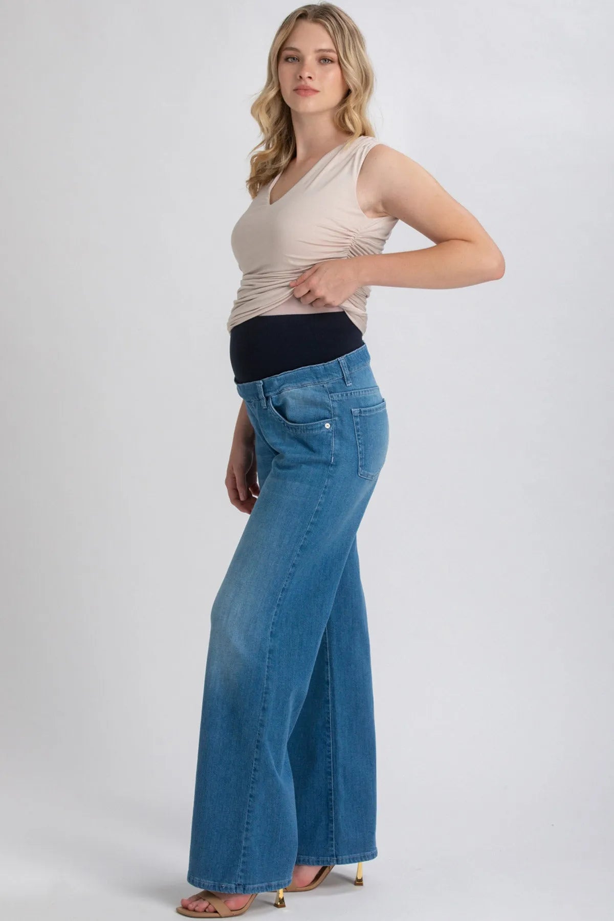 Donna incinta indossa jeans premaman a zampa con fascia elastica nera e top beige.