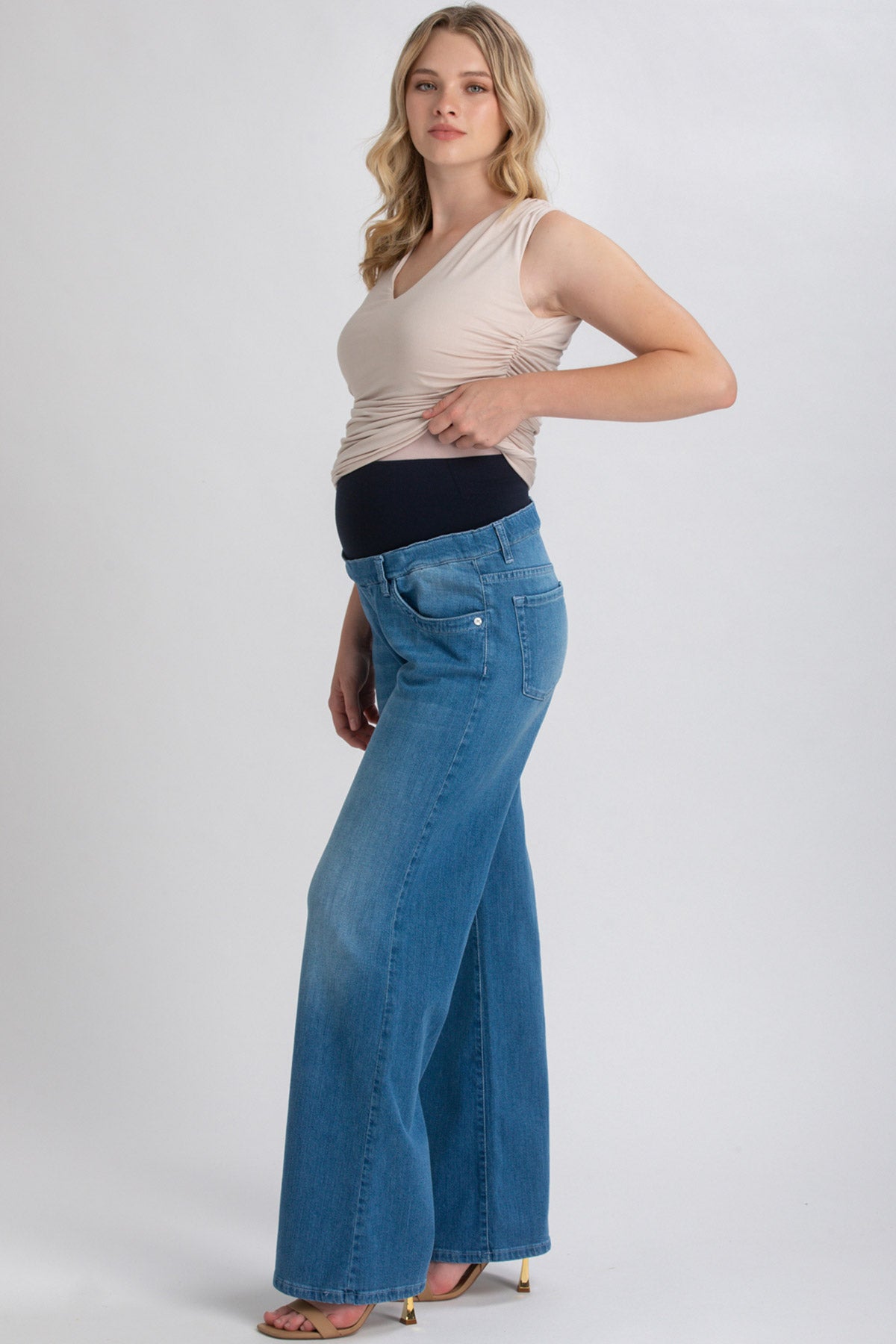 Donna incinta indossa jeans premaman a zampa con fascia elastica nera e top beige.