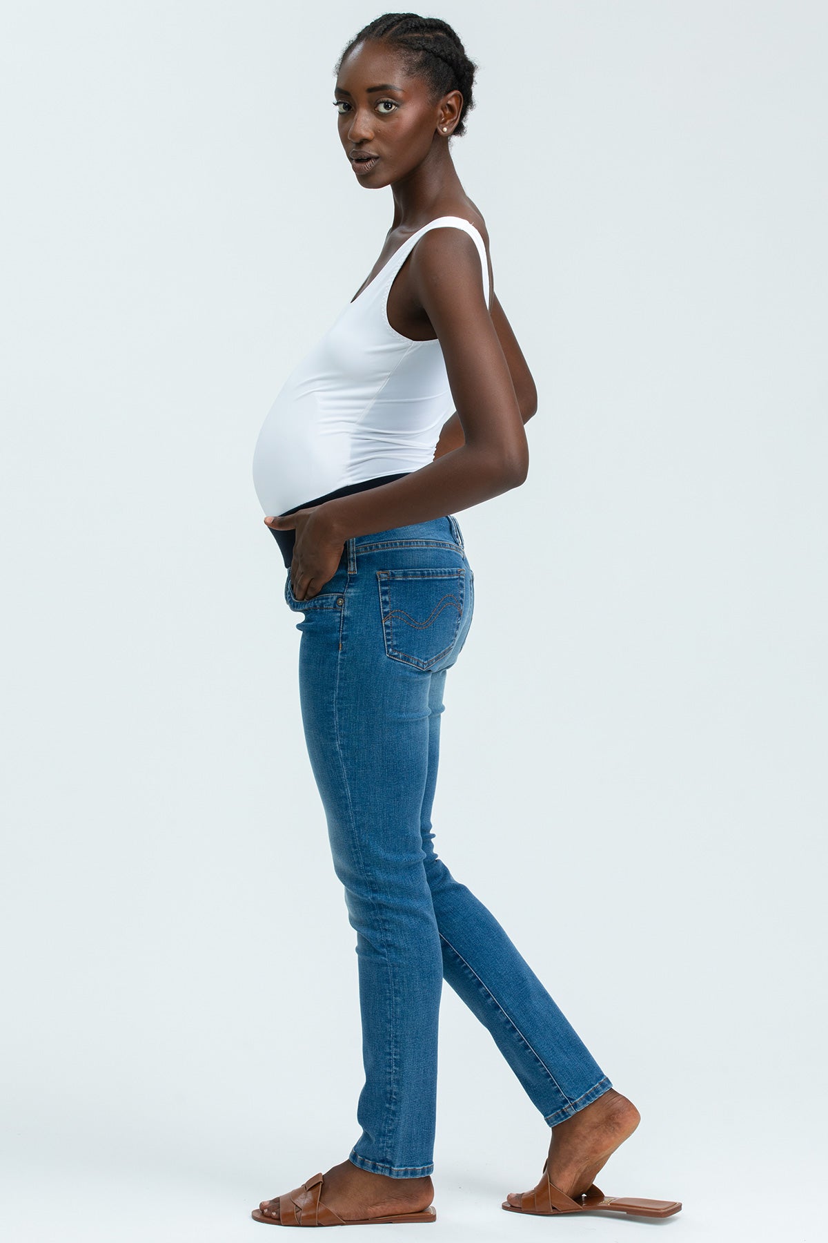 Modella incinta indossa jeans premaman elasticizzati e canotta bianca su sfondo neutro