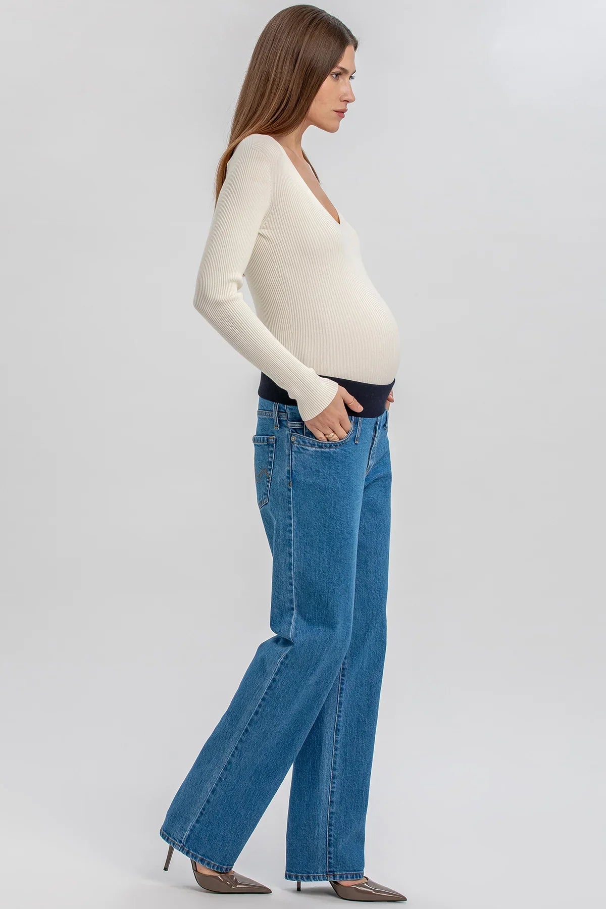 Modella con jeans premaman blu a vita alta e maglia a costine color panna con maniche lunghe.