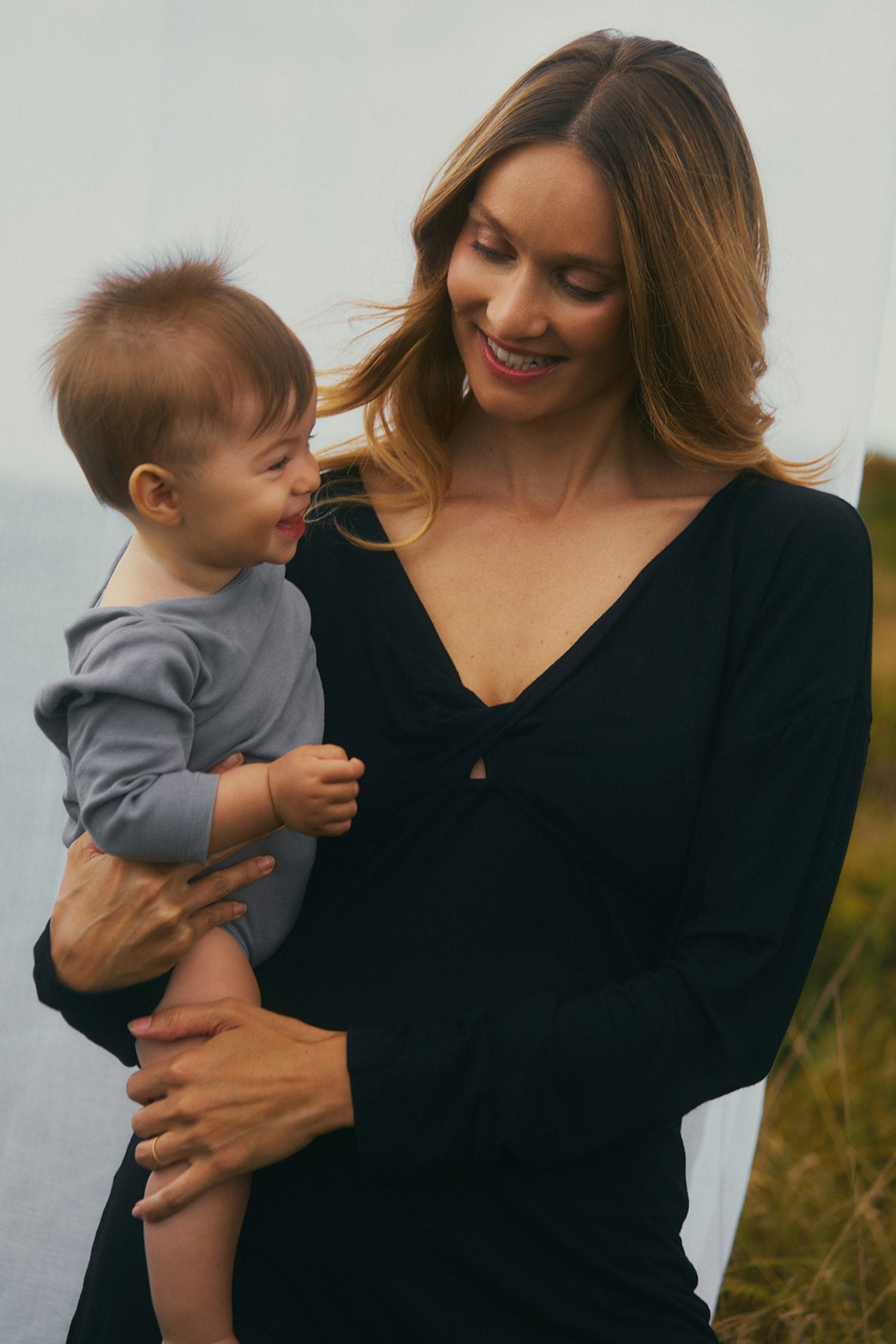 Abito premaman nero elegante con scollo a V indossato da una mamma che tiene in braccio un bambino.