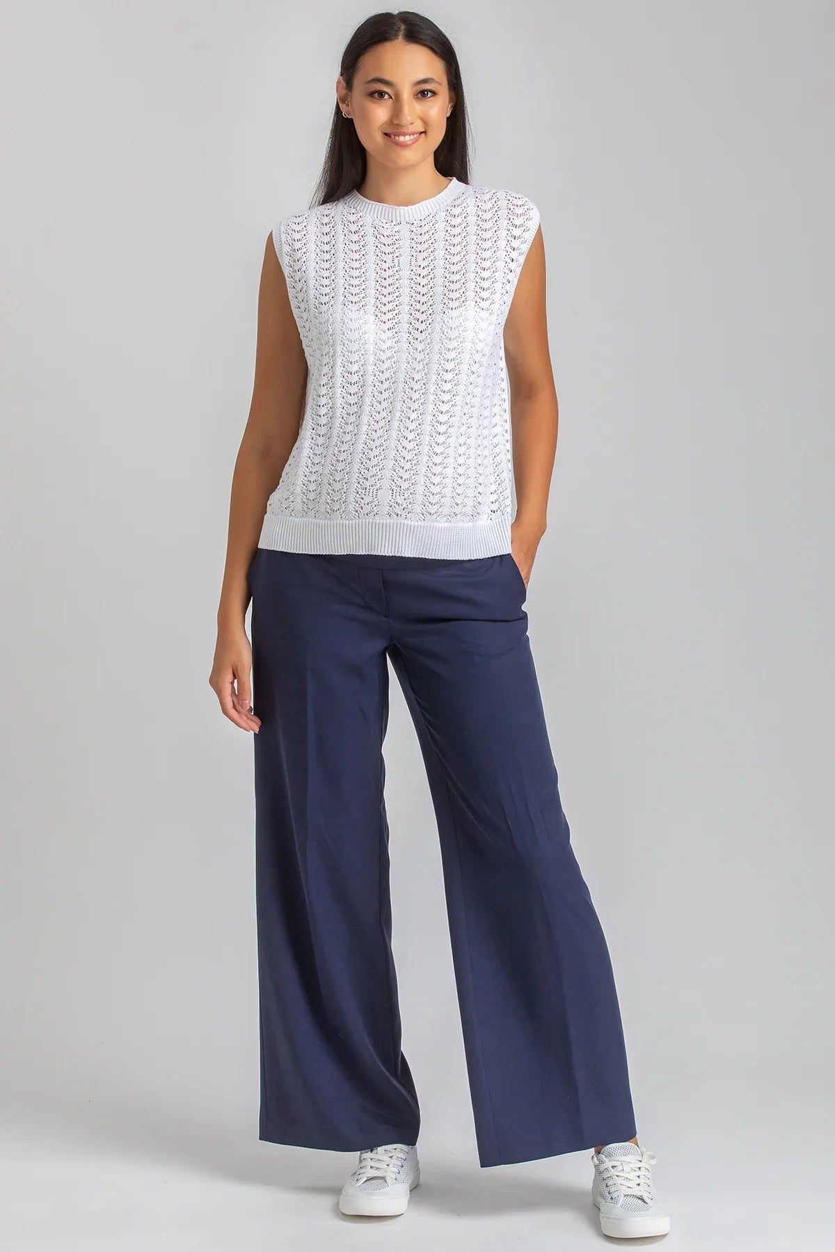 Modella indossa top premaman bianco traforato e pantaloni blu ampi, look premaman elegante