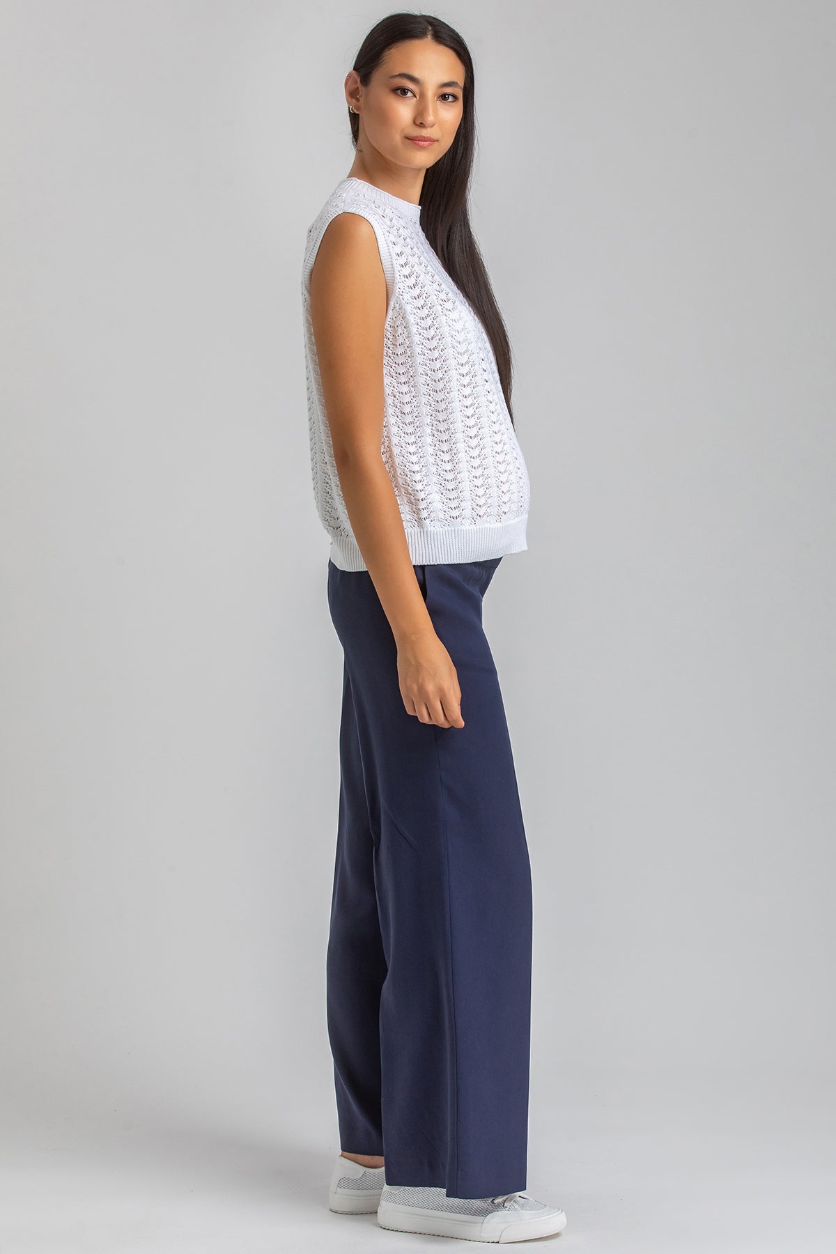Modella con abbigliamento premaman, maglia smanicata bianca e pantaloni blu, posa laterale
