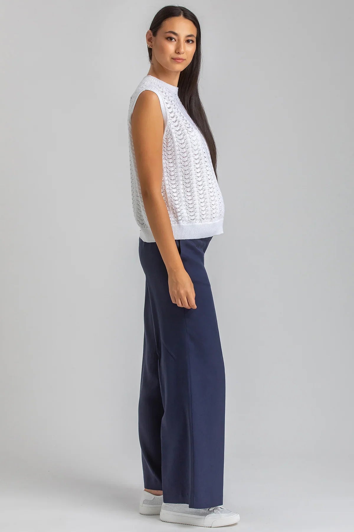 Modella con abbigliamento premaman, maglia smanicata bianca e pantaloni blu, posa laterale