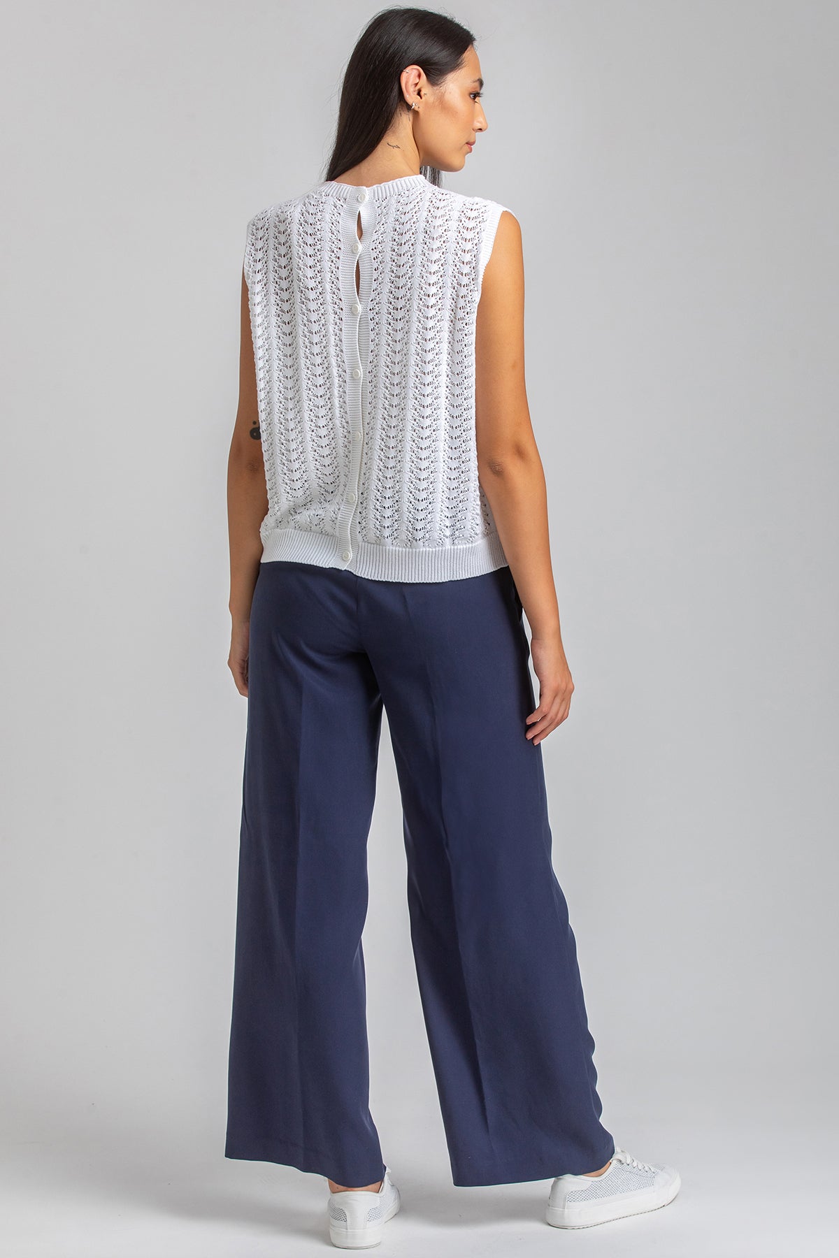 Donna di profilo con maglia premaman traforata bianca e pantaloni blu larghi