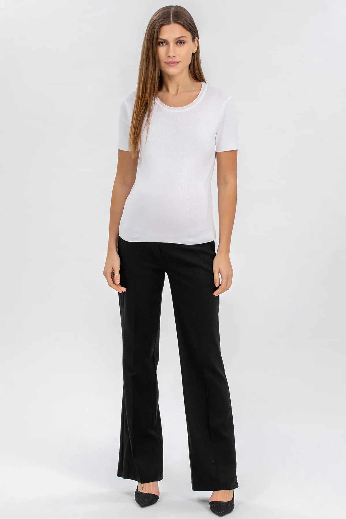Donna con maglietta premaman bianca e pantaloni neri eleganti, sfondo neutro