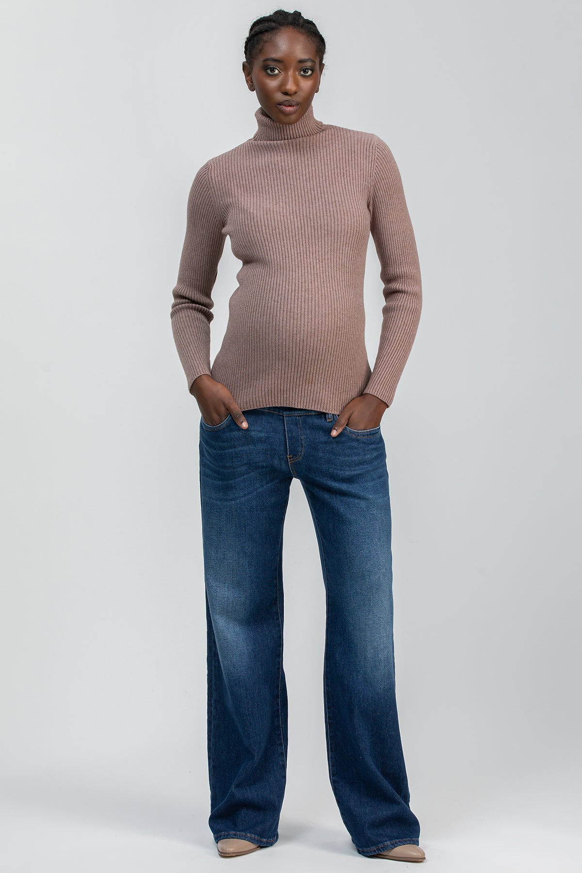 Modella indossa maglione premaman a coste beige e jeans a gamba larga, look casual.