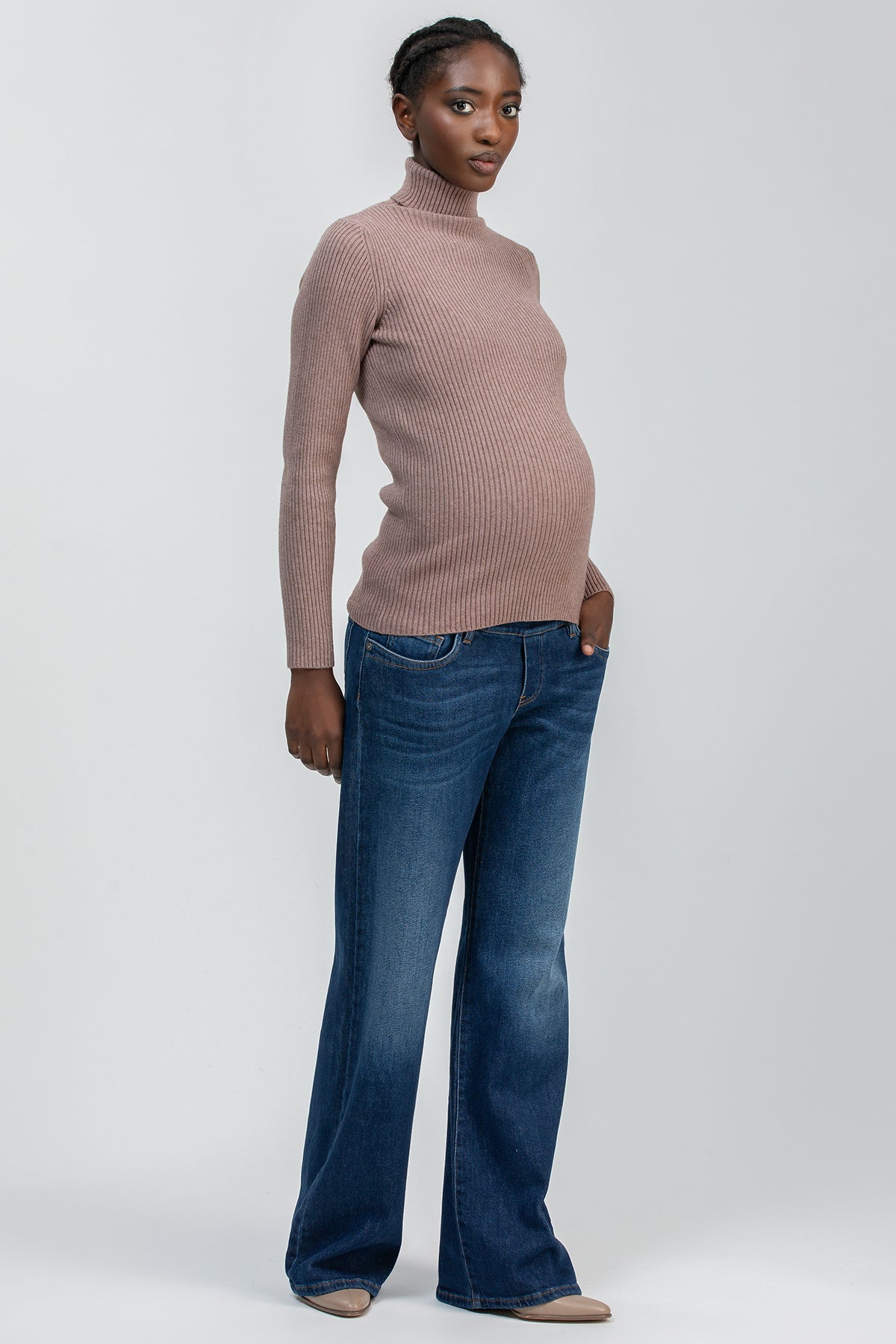 Modella incinta con maglione premaman a collo alto rosa e jeans flare in denim