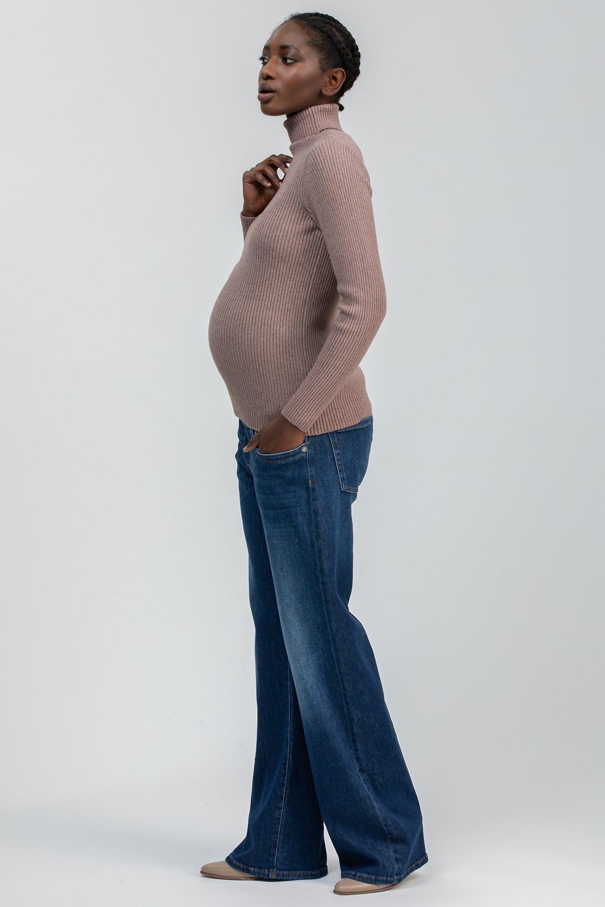 Modella incinta con maglione premaman a collo alto beige e jeans ampi, abbigliamento premaman elegante