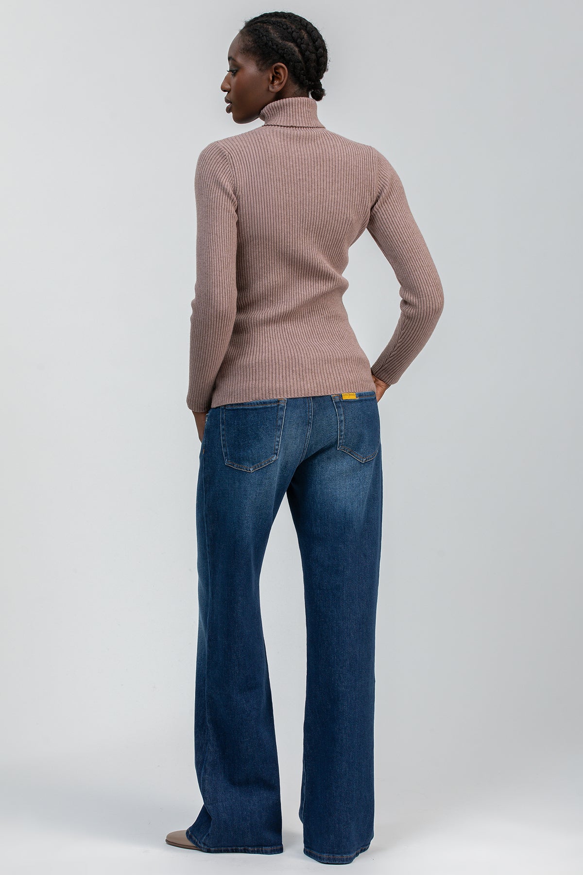 Donna con maglione premaman a collo alto beige e jeans premaman svasati, vista posteriore