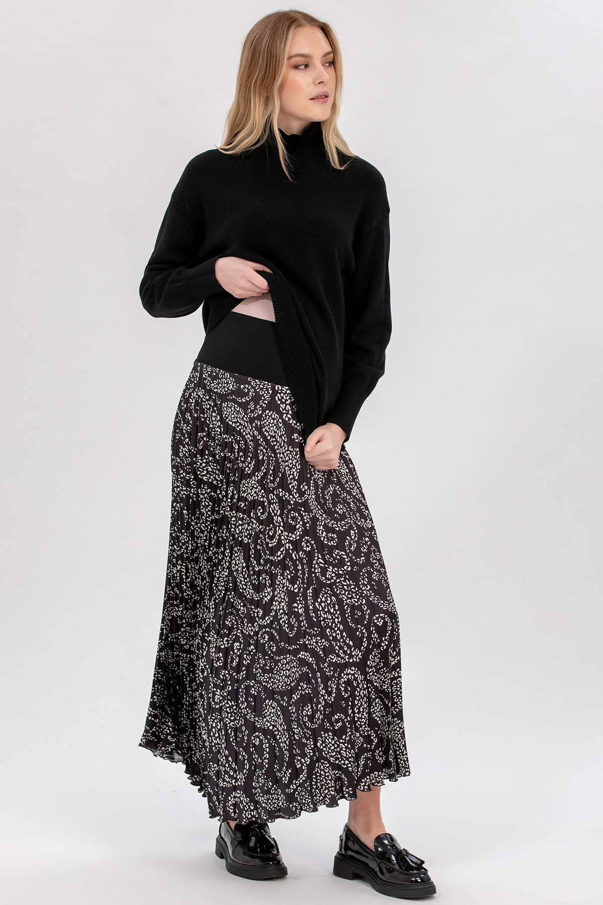 Donna con maglione nero e gonna premaman lunga a fantasia, moda abbigliamento premaman elegante.