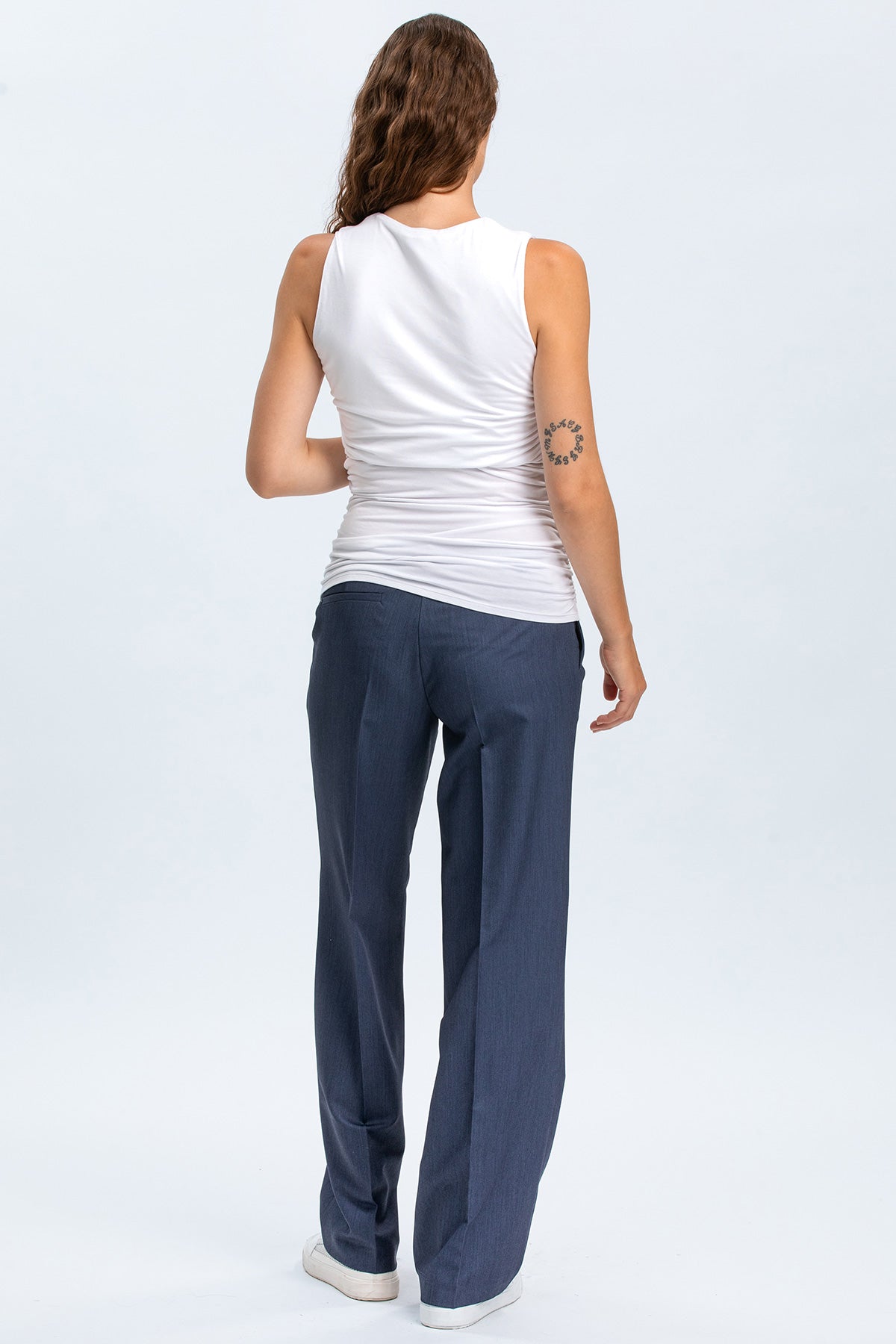 Modella vista da dietro con pantaloni premaman eleganti blu e top bianco senza maniche