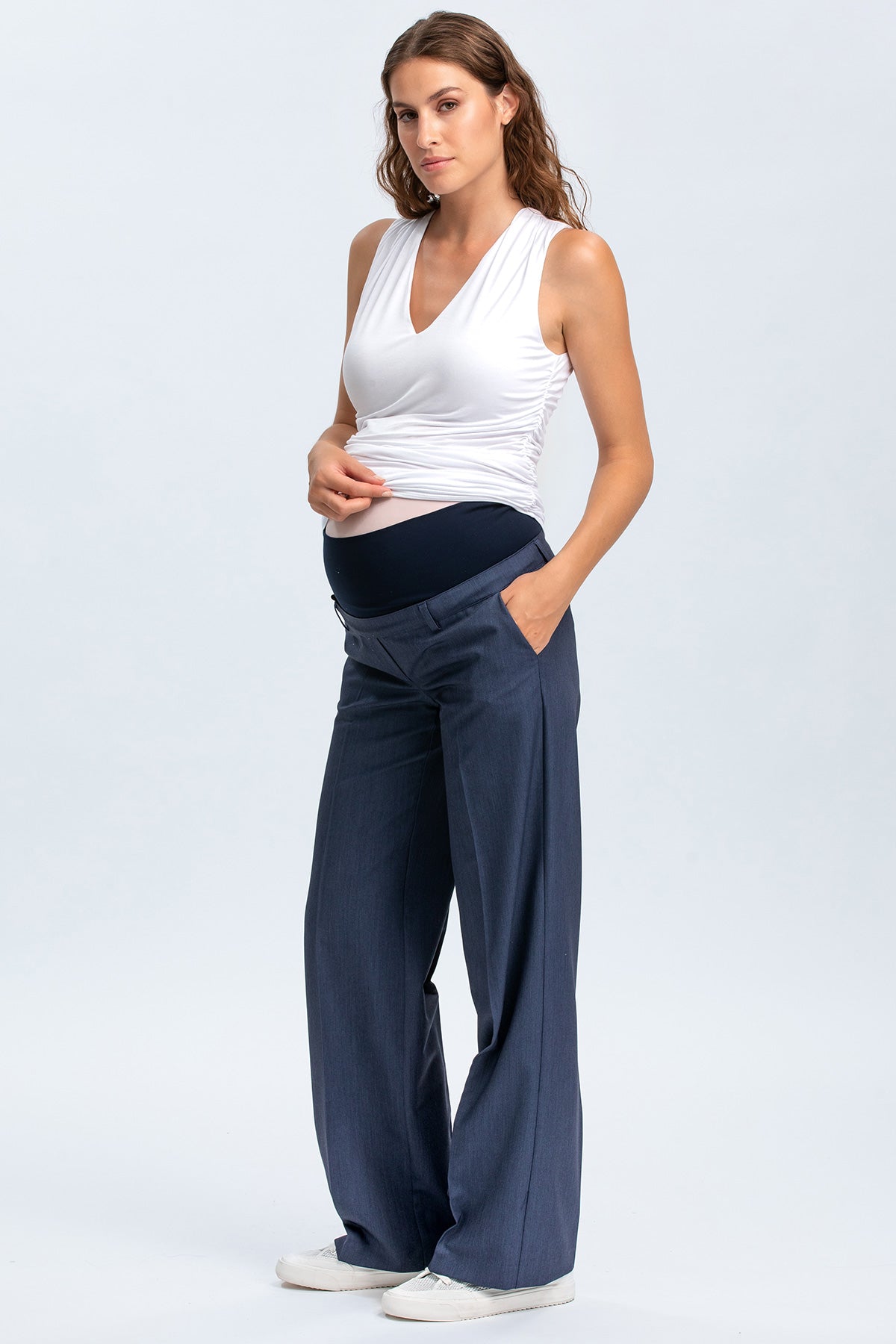 Donna incinta con pantaloni premaman blu eleganti e top bianco senza maniche