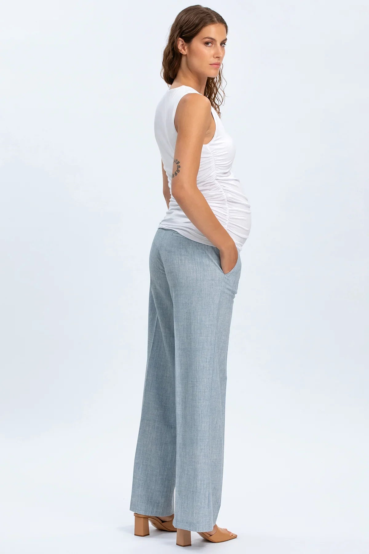 Donna incinta indossa top premaman bianco e pantaloni premaman larghi azzurri eleganti