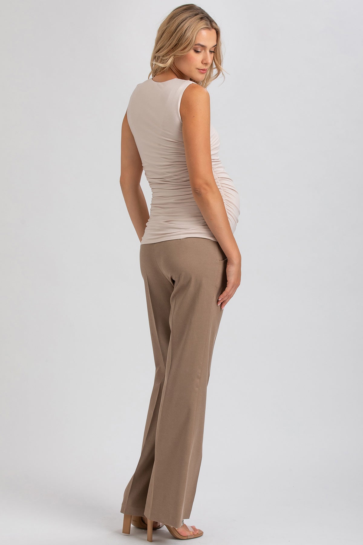 Donna incinta indossa top premaman beige senza maniche e pantaloni eleganti color sabbia.