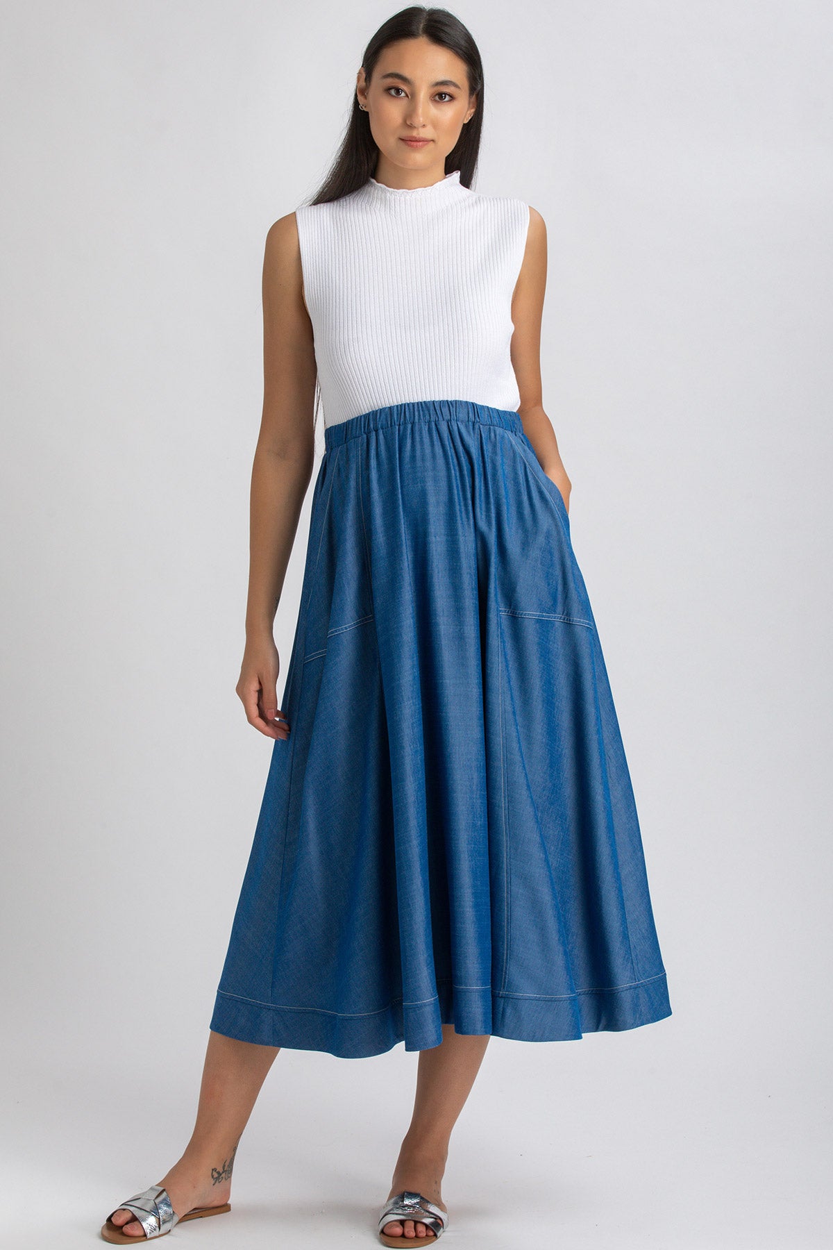 Donna con abito premaman smanicato bianco e gonna lunga blu, sandali flat, fondo neutro
