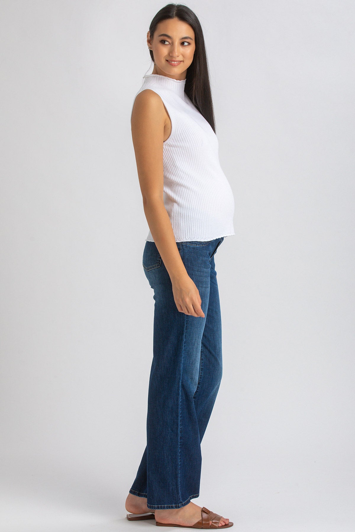 Modella incinta indossa top smanicato bianco e jeans premaman in denim blu