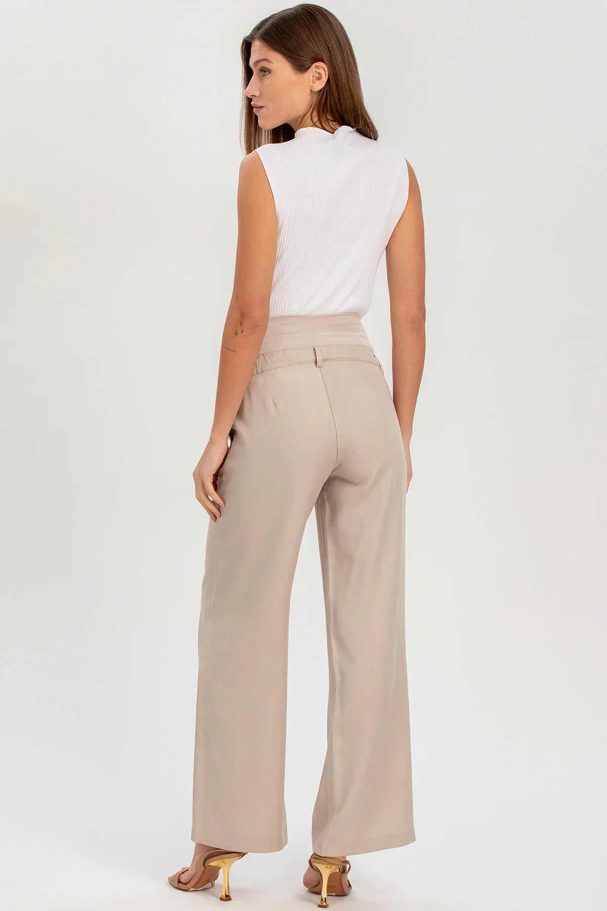 Donna in pantaloni premaman beige a gamba larga e top smanicato bianco, vista da dietro