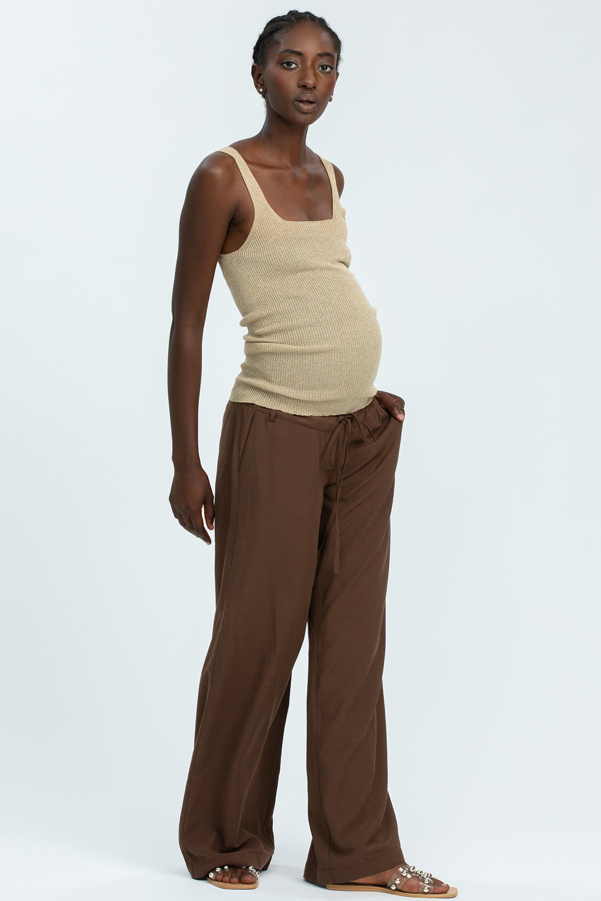 Modella indossa outfit premaman con top beige e pantaloni larghi marroni, abbigliamento premaman elegante e confortevole.