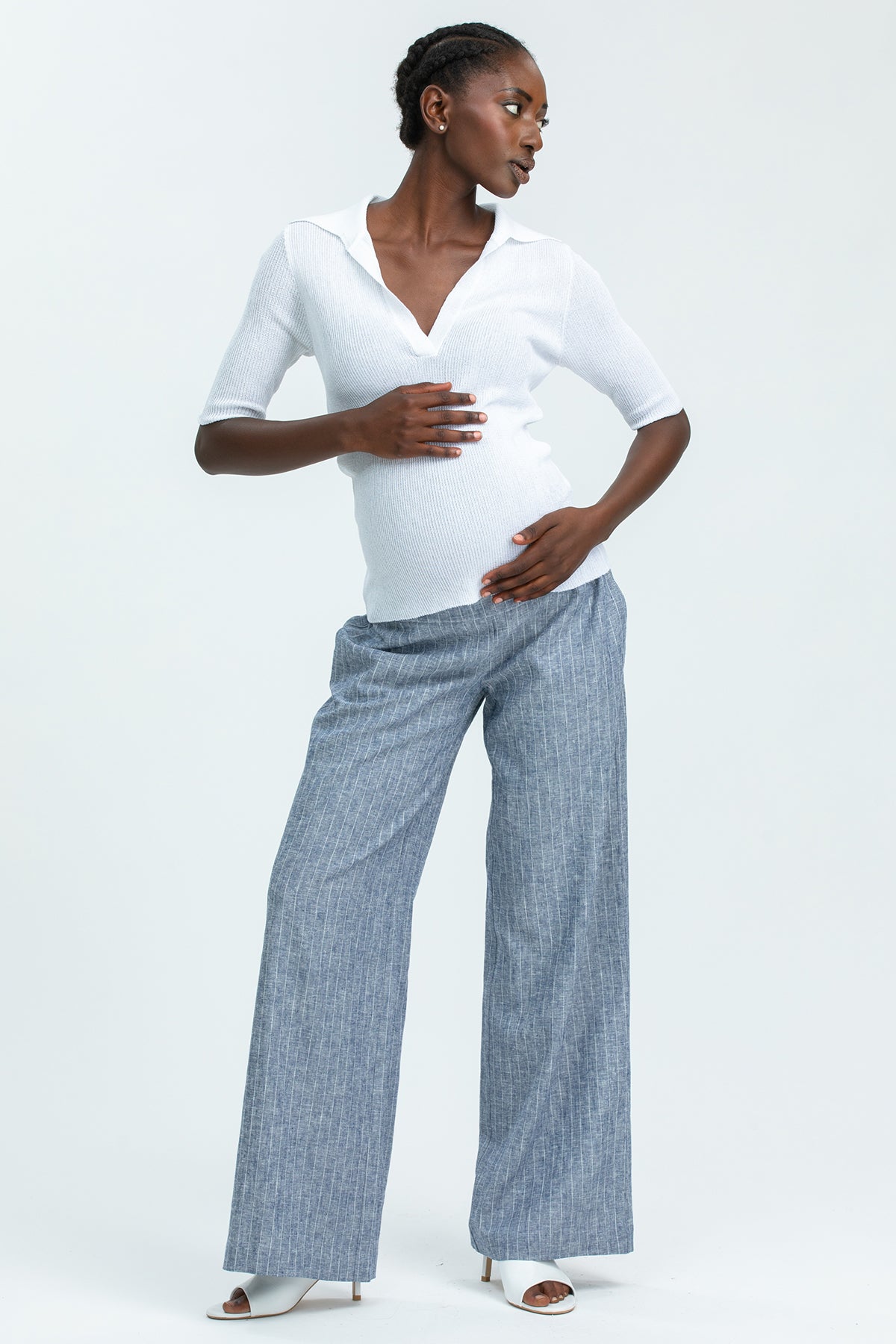 Donna incinta indossa pantaloni premaman larghi grigi e maglia premaman bianca elegante