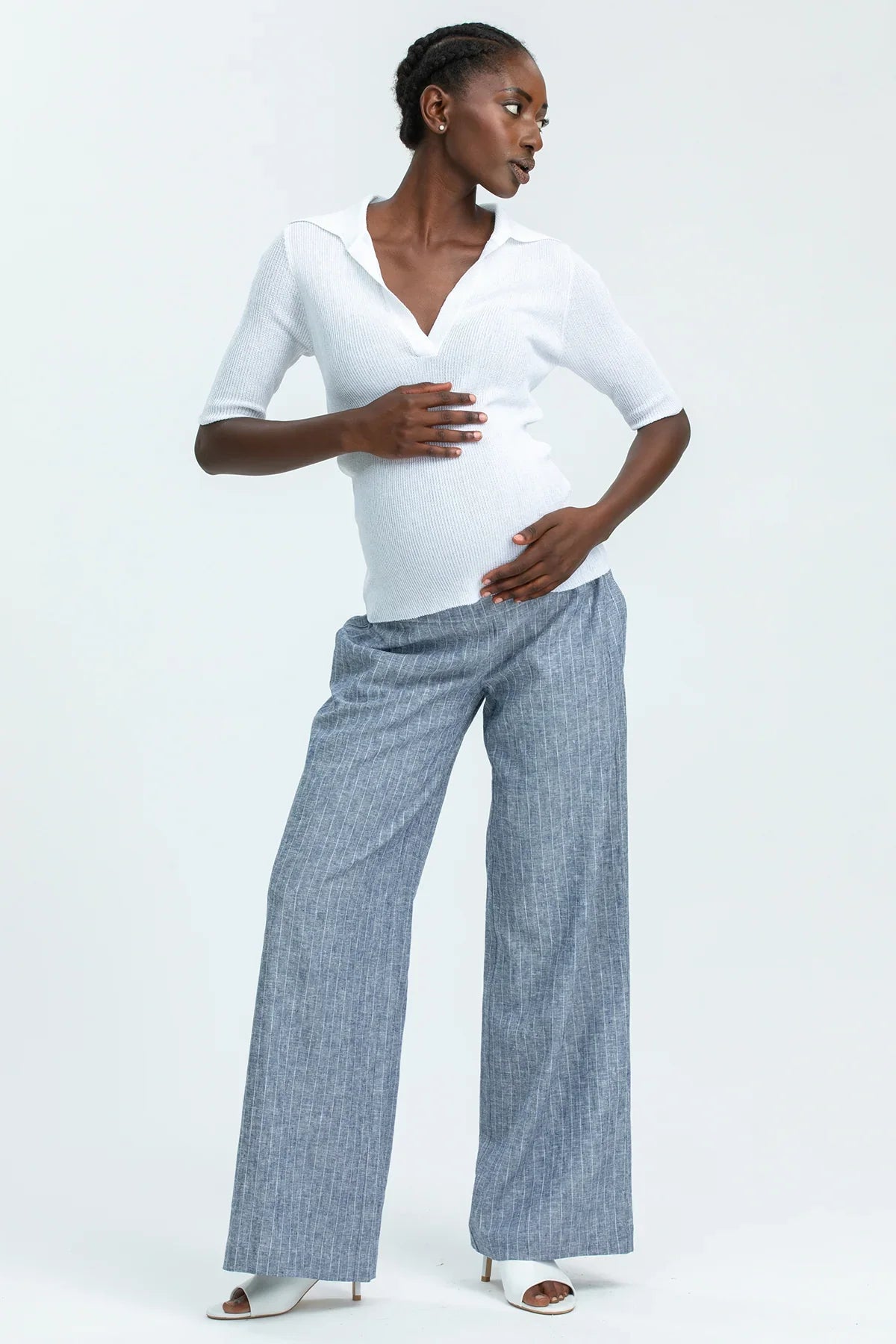 Donna incinta indossa pantaloni premaman larghi grigi e maglia premaman bianca elegante