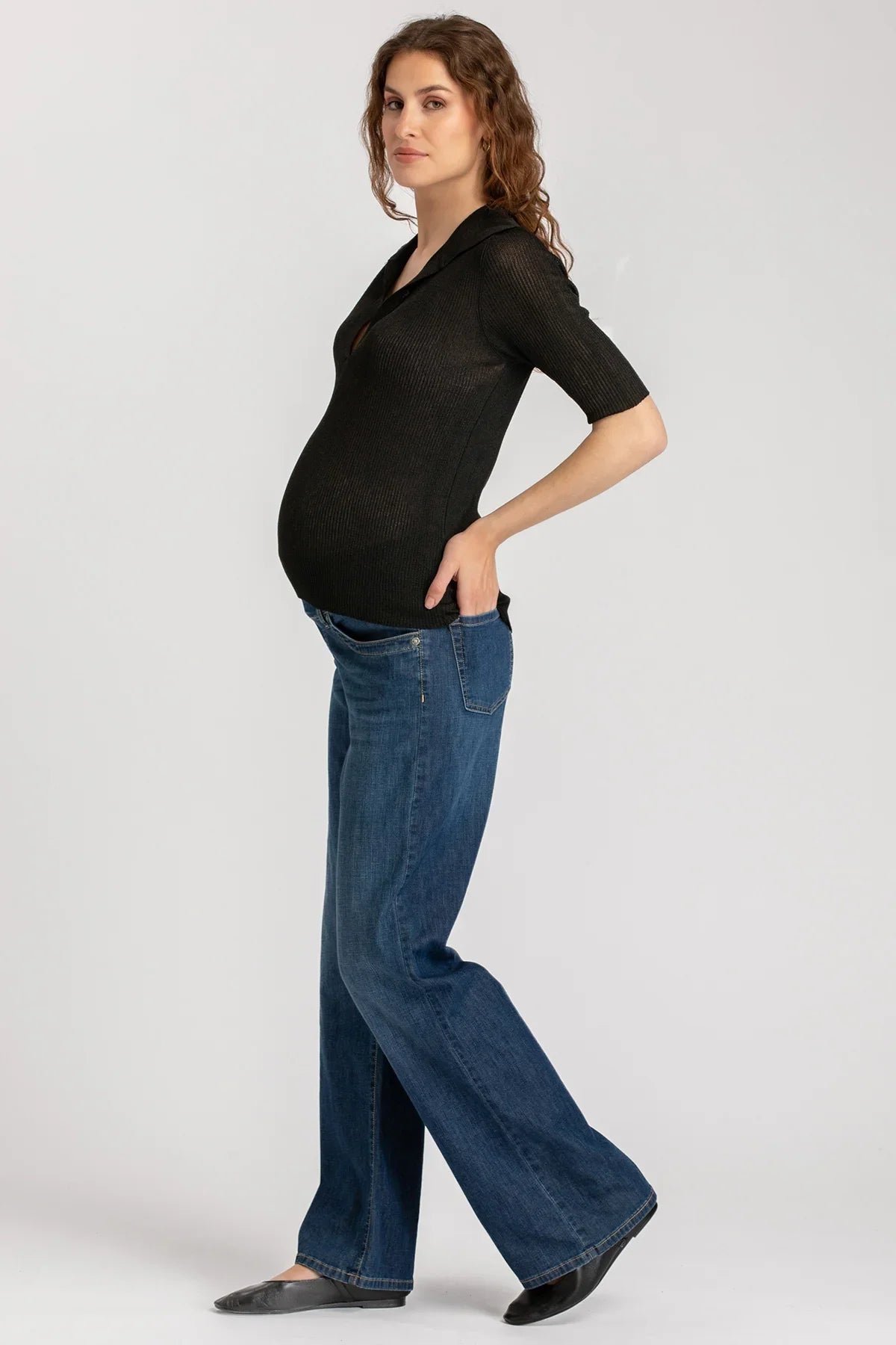 Donna incinta indossa top nero e jeans premaman su sfondo neutro, abbigliamento premaman casual