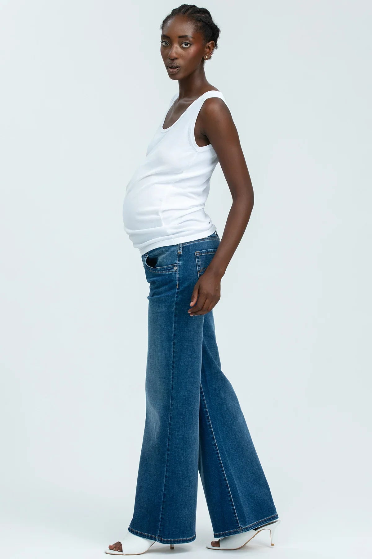 Donna incinta indossa top bianco premaman e jeans a gamba larga, stile moderno su sfondo neutro.