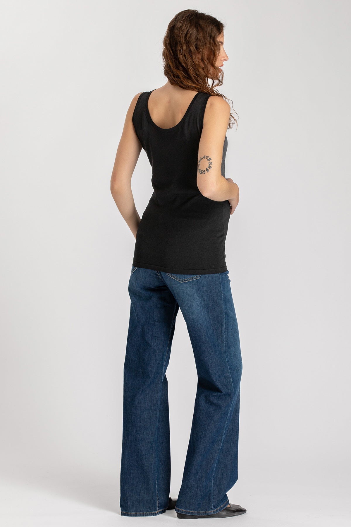 Donna di spalle con canotta nera premaman e jeans larghi, abbigliamento premaman casual.
