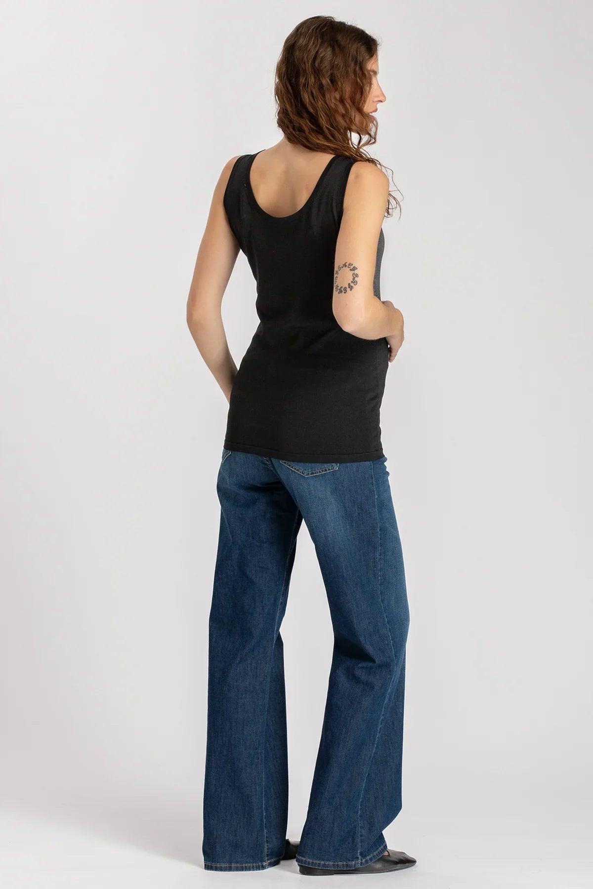 Donna di spalle con canotta nera premaman e jeans larghi, abbigliamento premaman casual.