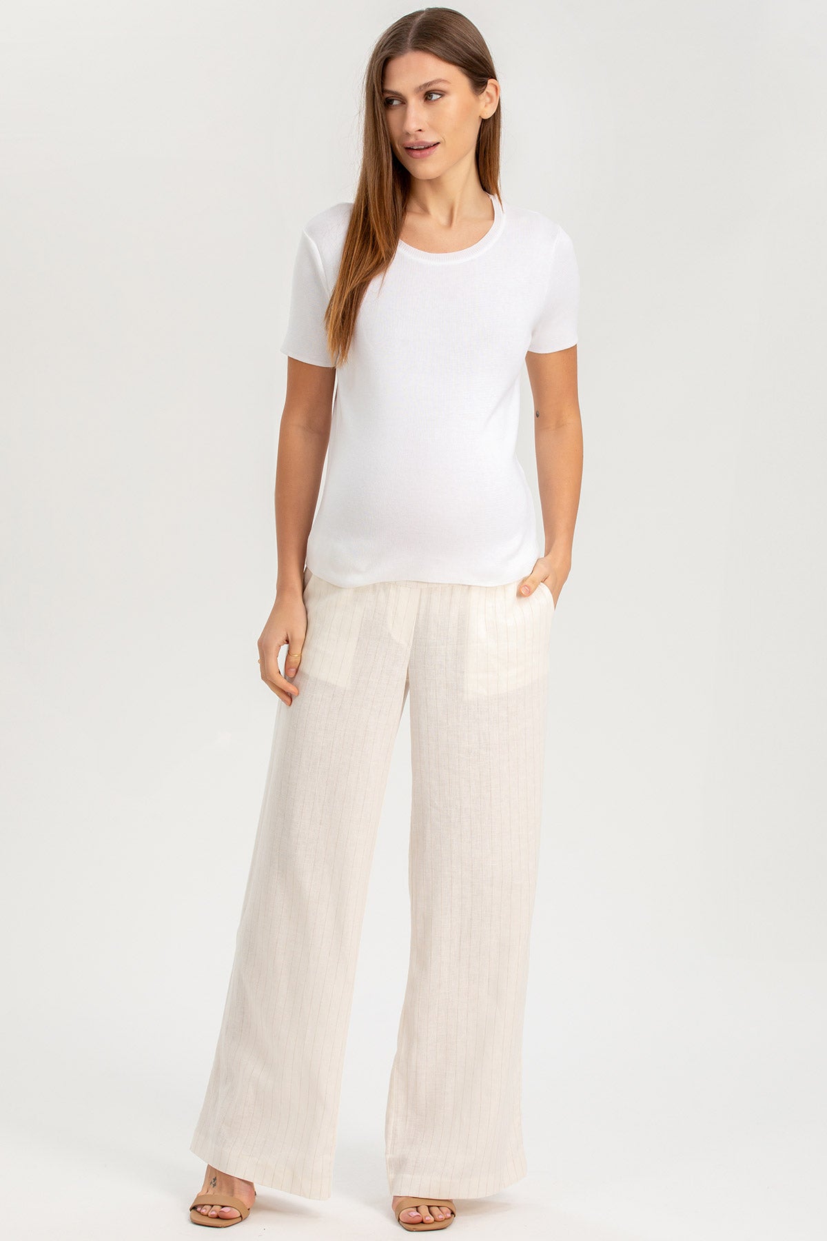 Donna incinta con t-shirt bianca premaman e pantaloni ampi chiari, look elegante e confortevole.