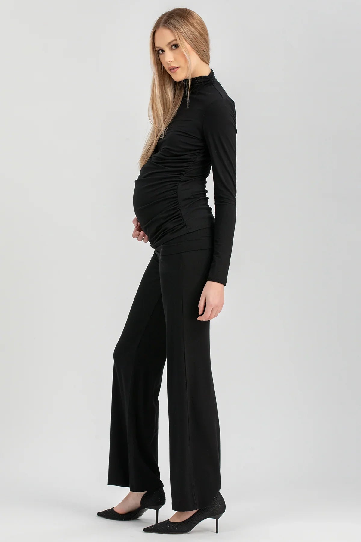 Modella premaman con pantaloni larghi e maglia nera eleganti, look sofisticato.