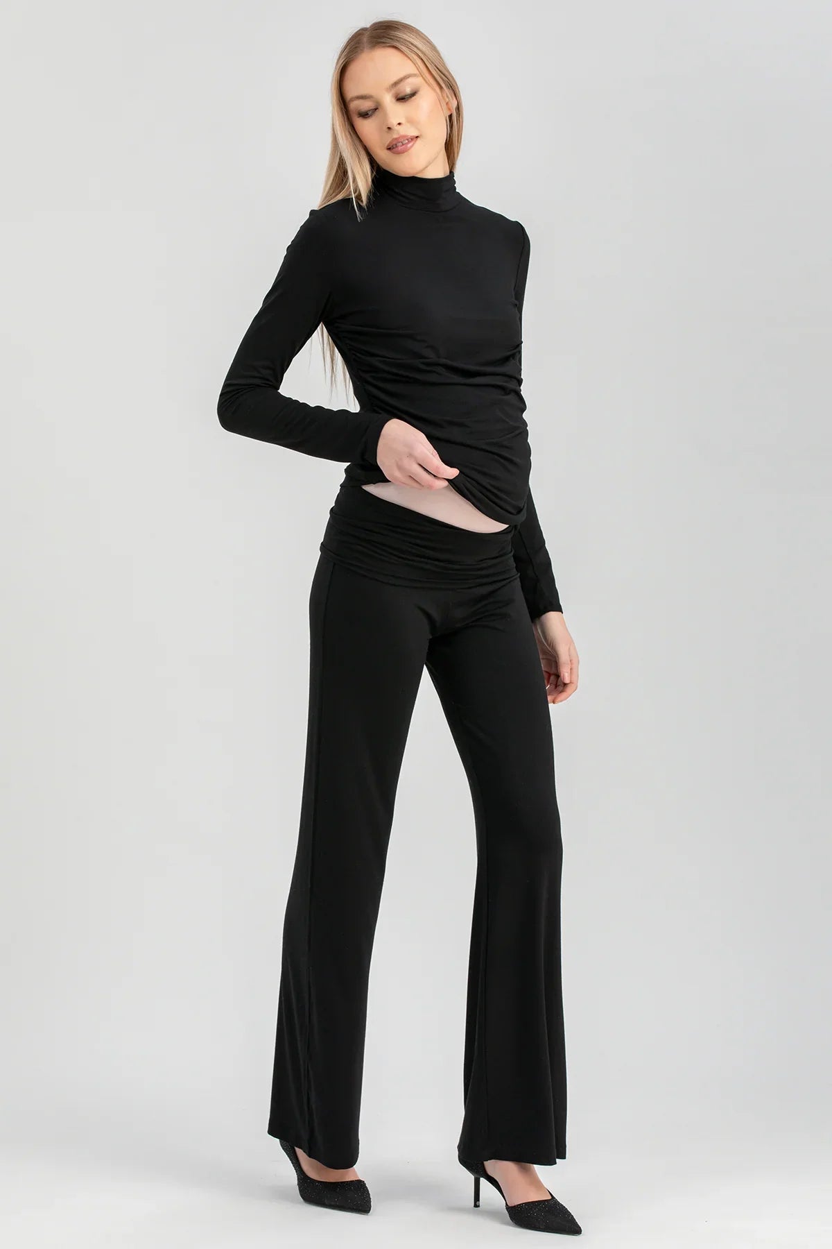 Modella indossa completo premaman nero elegante con pantaloni a zampa e maglia a collo alto