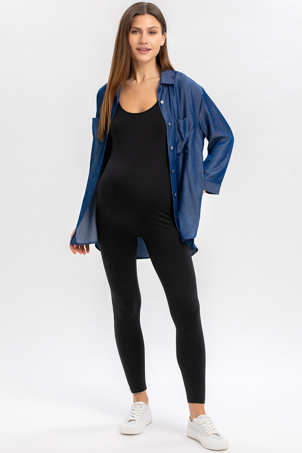 Donna incinta con tuta premaman nera e camicia di jeans blu, look casual confortevole