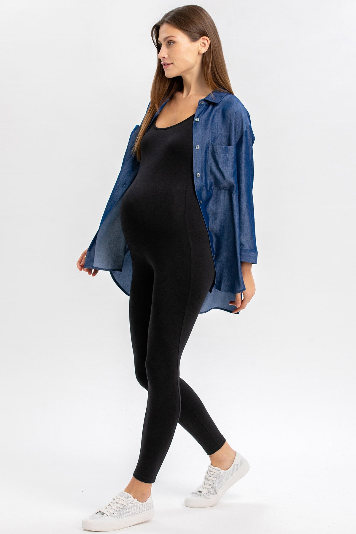 Modella incinta con leggings premaman neri e camicia in denim, look casual elegante