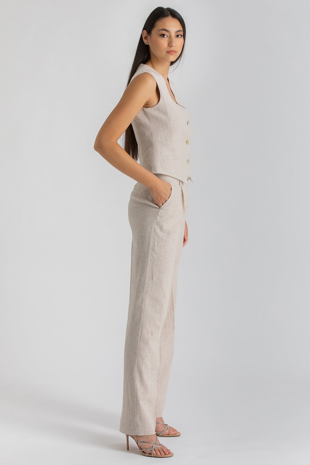 Donna indossa completo premaman lino beige, top senza maniche e pantaloni eleganti.