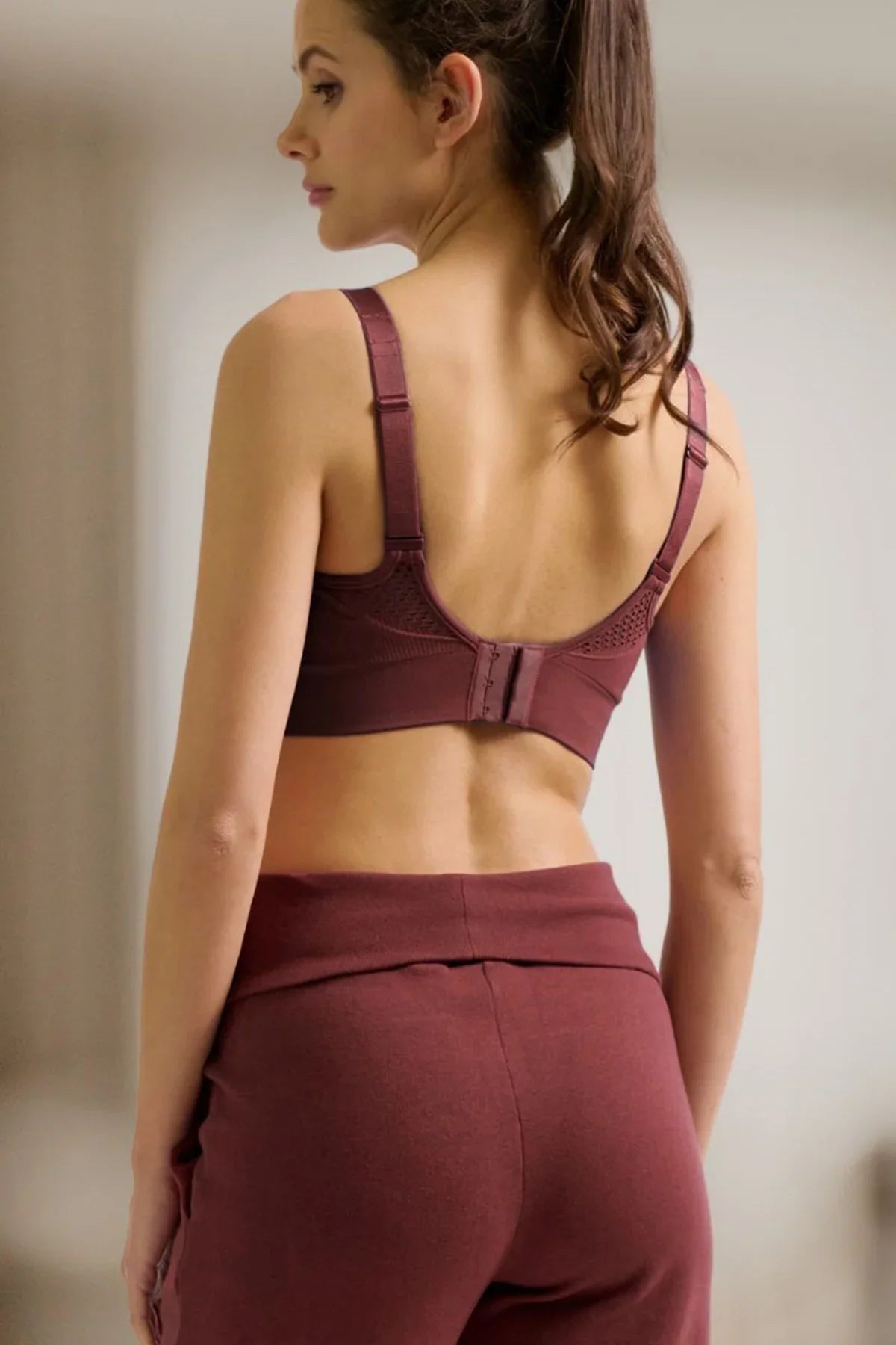 Donna di profilo con reggiseno e pantaloni premaman bordeaux, abbigliamento premaman comodo