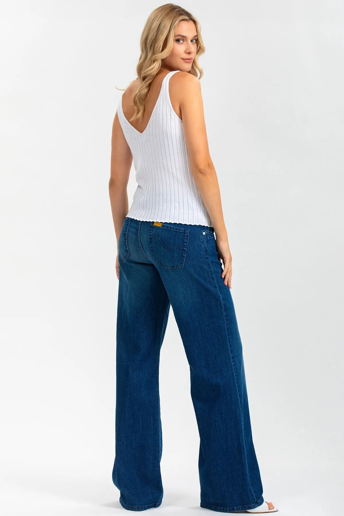 Donna con top bianco senza maniche e jeans premaman ampi in posa su sfondo chiaro