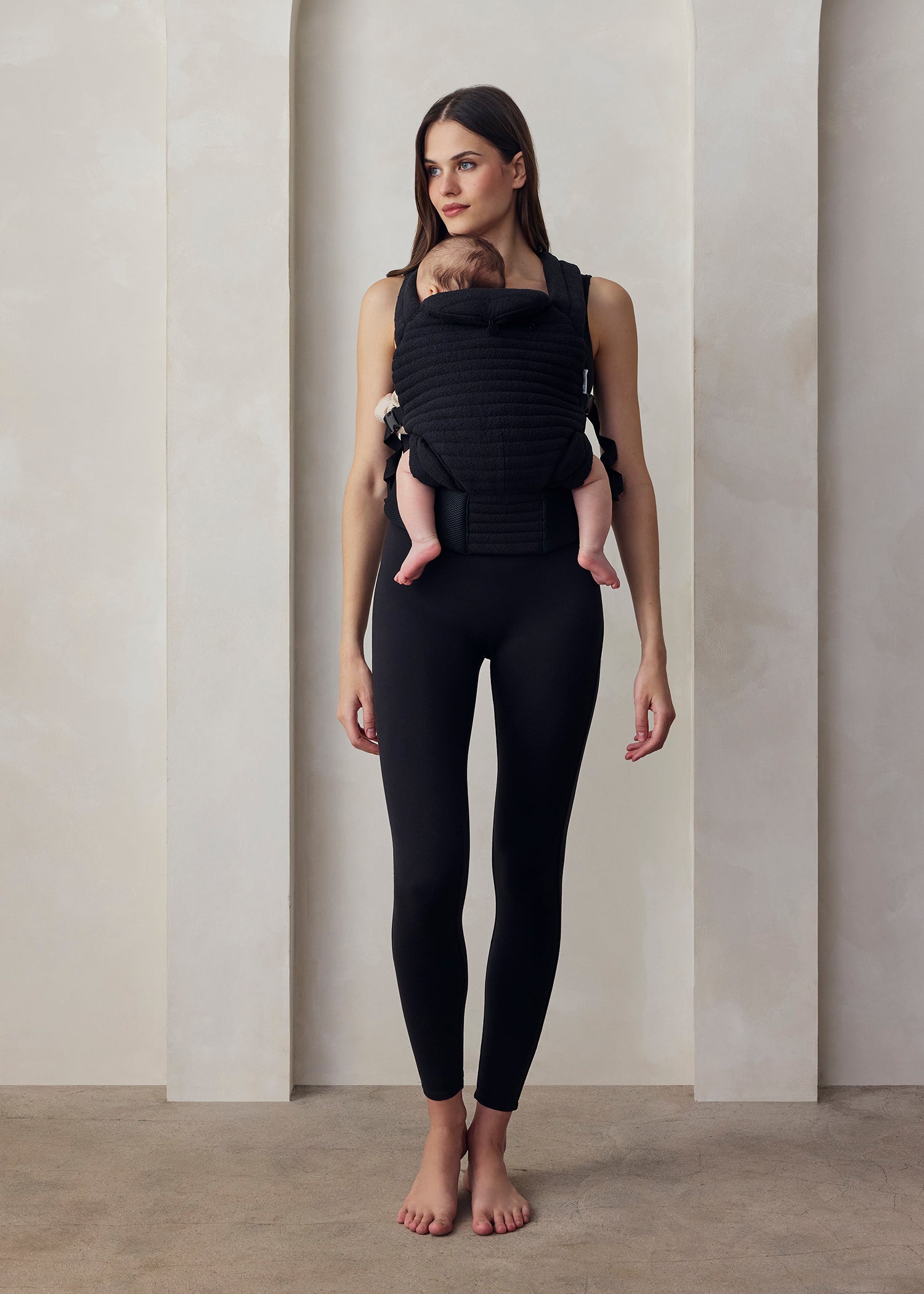 Donna con abbigliamento premaman nero e marsupio porta bebè, ambiente minimal