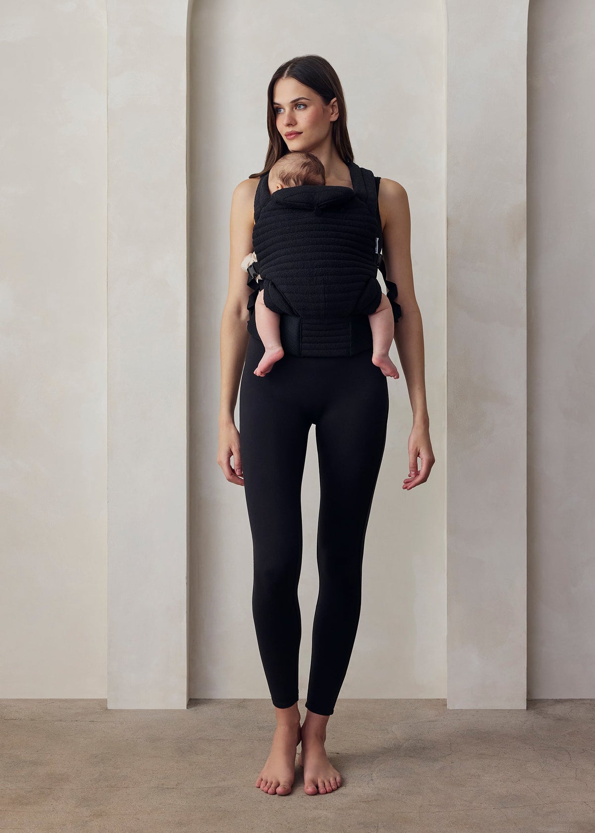 Donna con abbigliamento premaman nero e marsupio porta bebè, ambiente minimal