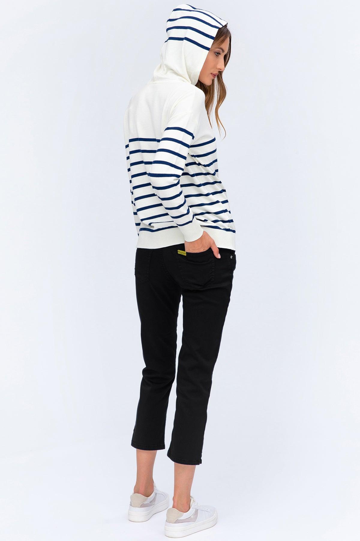 Donna con felpa premaman a righe bianche e blu, pantaloni neri e sneakers bianche