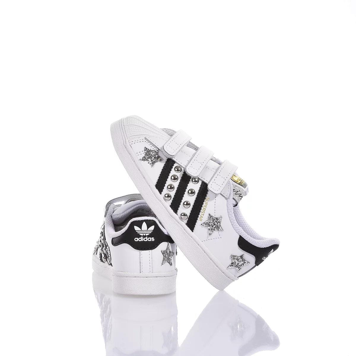 Scarpe da ginnastica bianche con decorazioni a stelle glitterate e borchie, fondo bianco riflettente.