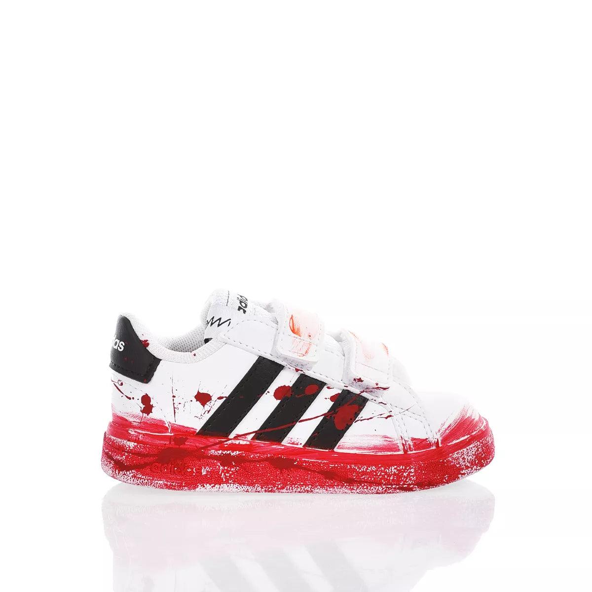 Sneaker bianca Adidas con dettagli neri, schizzi di vernice rossa e chiusura a strappo