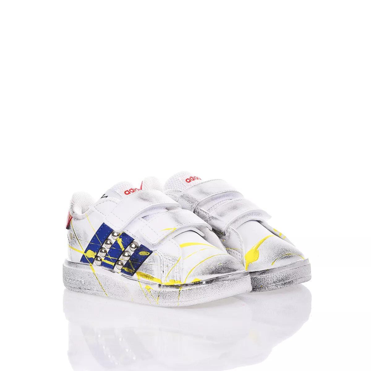 Scarpe da ginnastica bianche bambino con strisce blu, dettagli gialli e borchie, chiusura velcro.