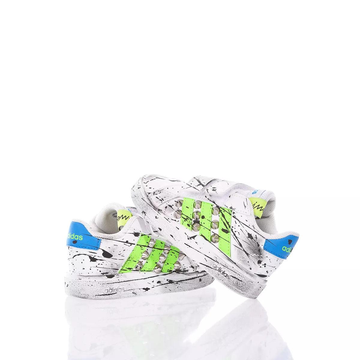 Scarpe da ginnastica bianche con dettagli verde fluo, blu e spruzzi neri, su sfondo bianco.