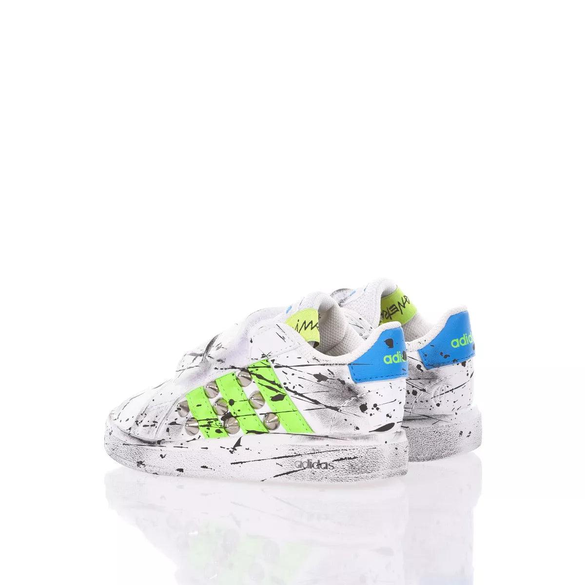 Scarpe sportive bianche con dettagli verdi e blu, effetto macchie di vernice nere.