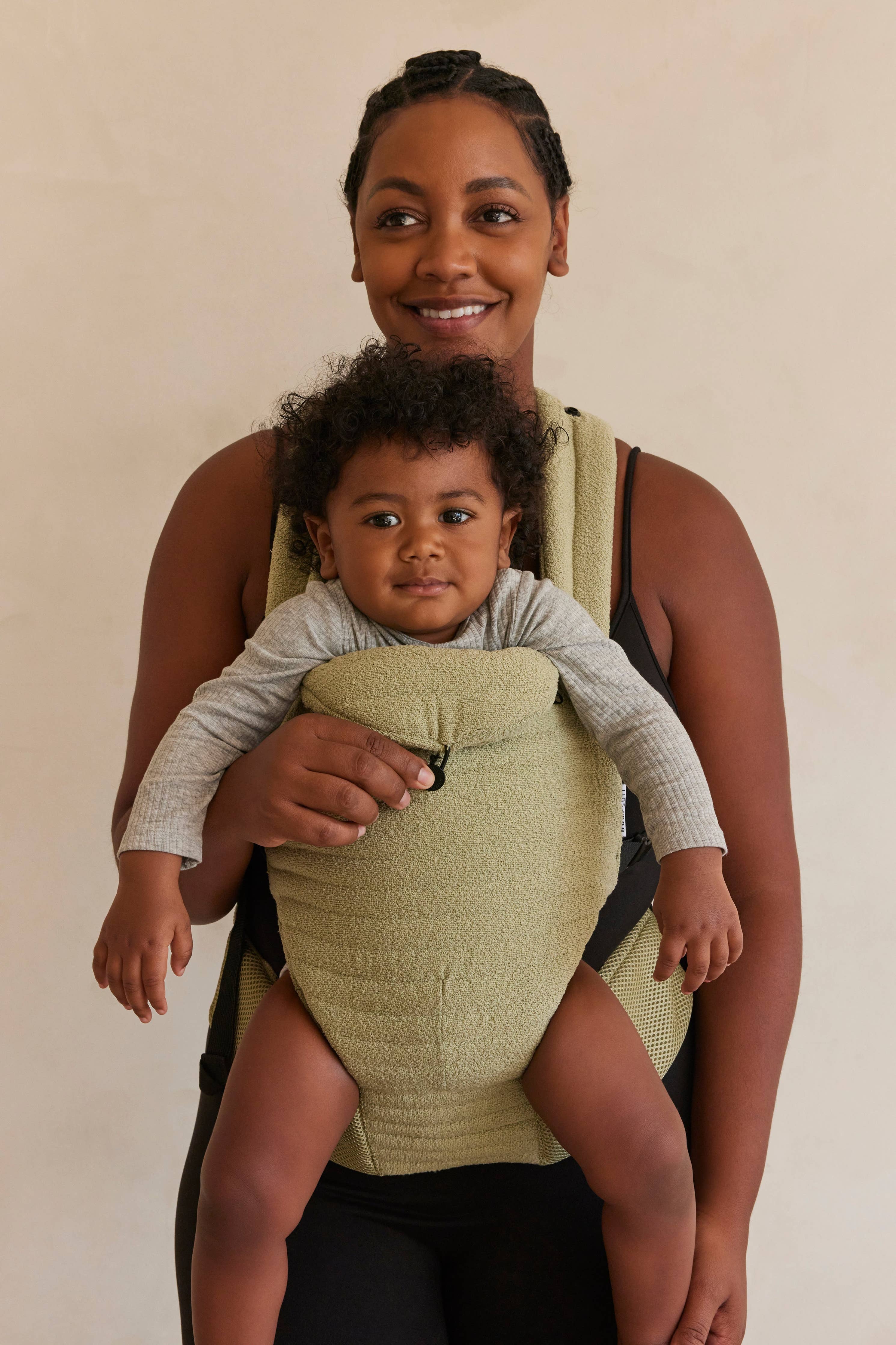 Mamma sorridente con marsupio premaman beige e bambino, abbigliamento gravidanza