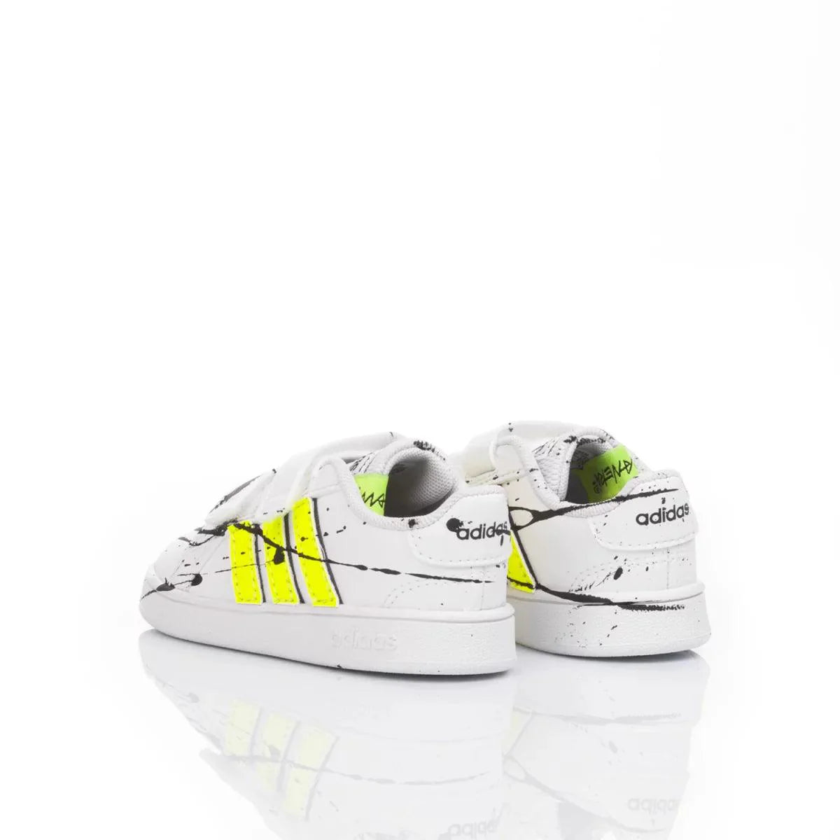 Scarpe da ginnastica bianche per bambini con dettagli gialli e schizzi neri, fondo riflettente.