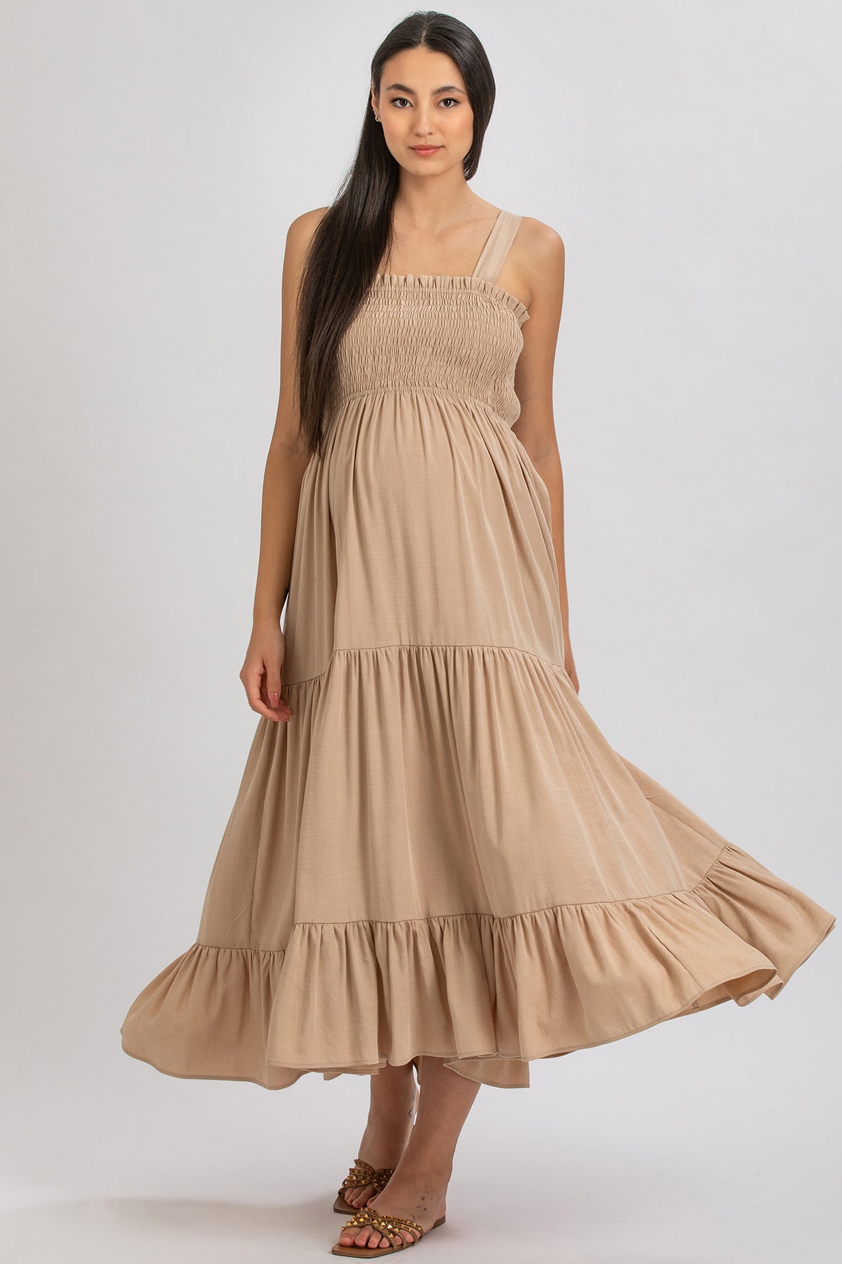 Abito premaman lungo beige senza maniche, tessuto leggero e arricciato, moda maternità elegante.