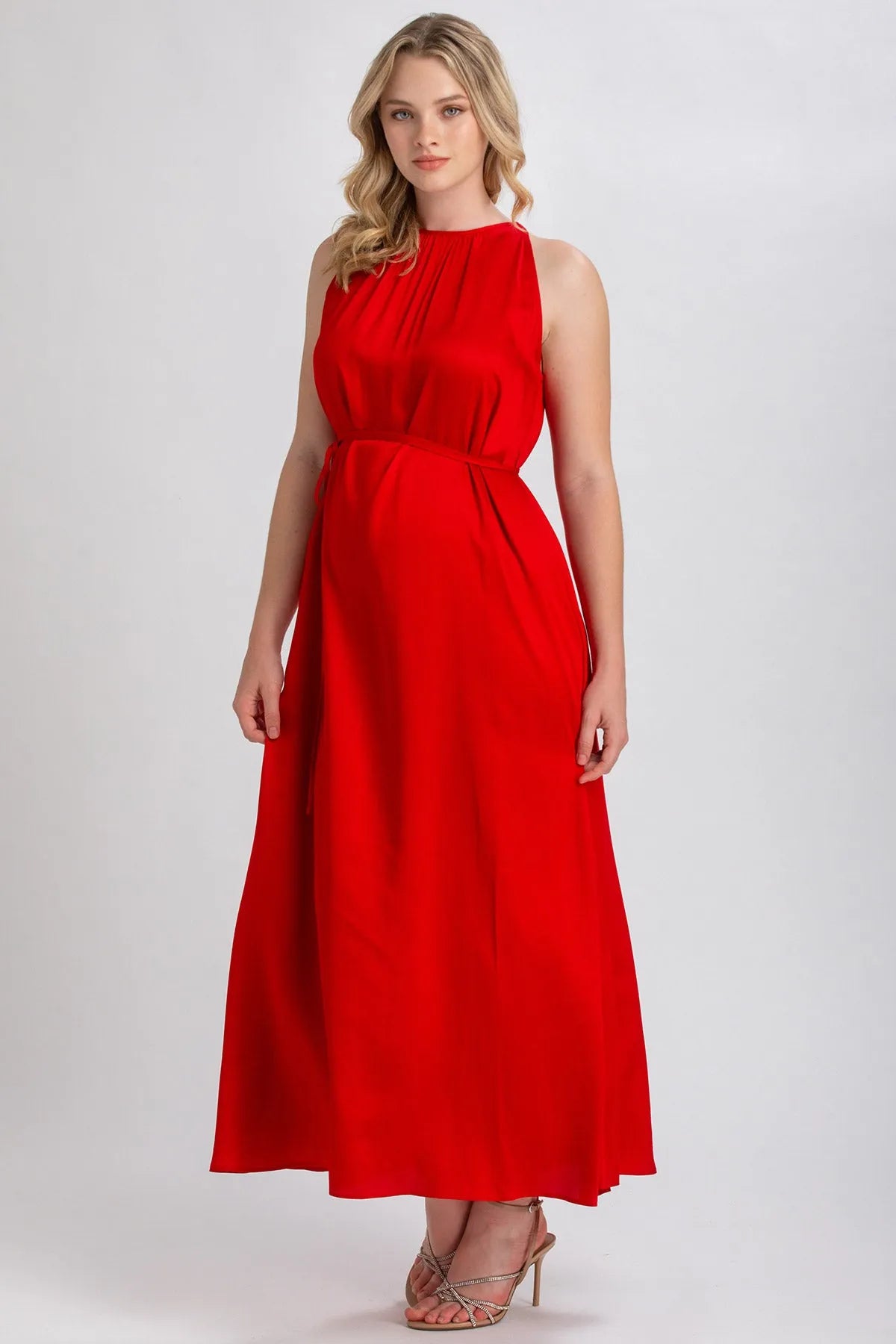 Donna incinta indossa elegante abito premaman lungo rosso senza maniche in studio.